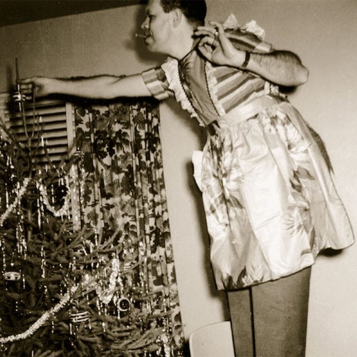 Man wearing a festive apron adding ornaments to a Christmas tree