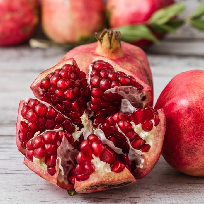 Half pomegranate and raw pomegranates on a white wooden background; Shutterstock ID 228369412
