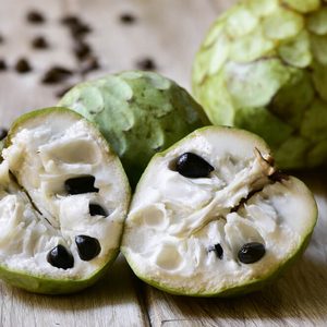 closeup of some custard apples, one of them cut in half, on a rustic wooden surface