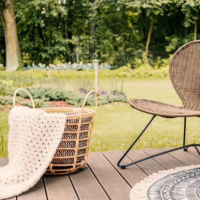 Close-up of a brown garden chair and a beige blanket in a basket on a wooden patio in the yard