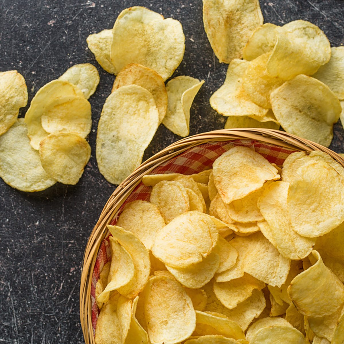 Crispy potato chips in a wicker bowl on old kitchen table