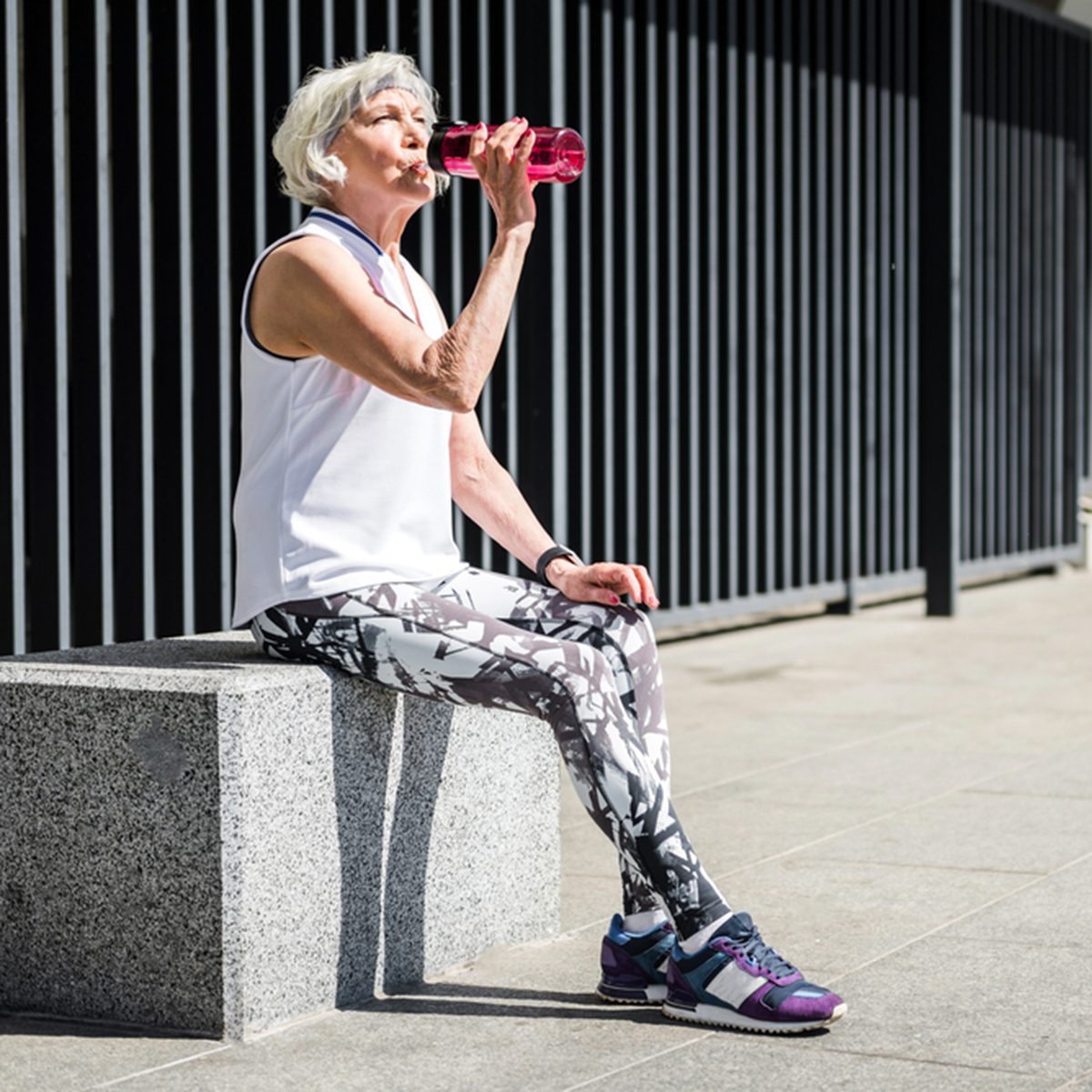 Tired senior lady having rest after exercise beside metal fence