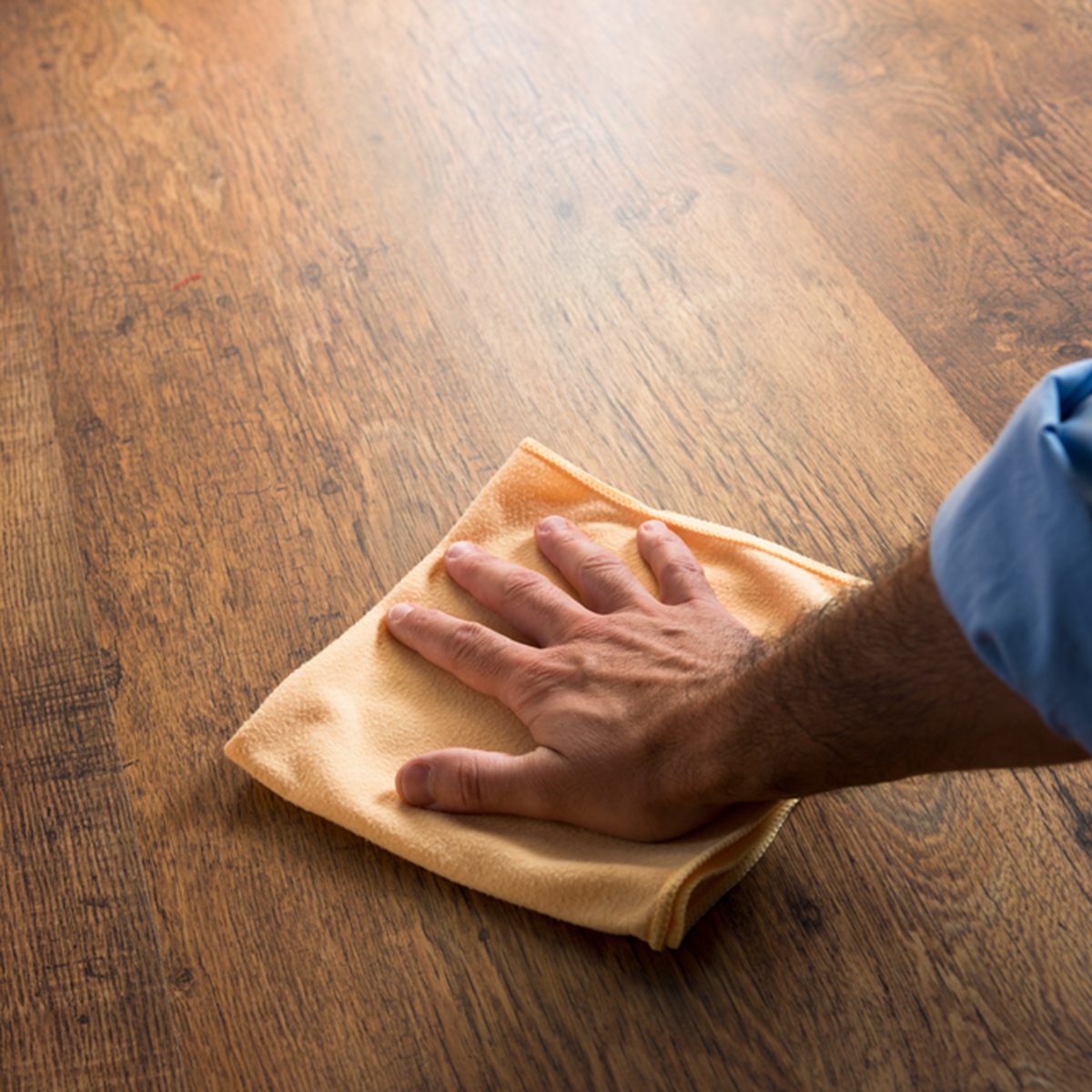 Male hand cleaning and rubbing an hardwood floor with a microfiber cloth.