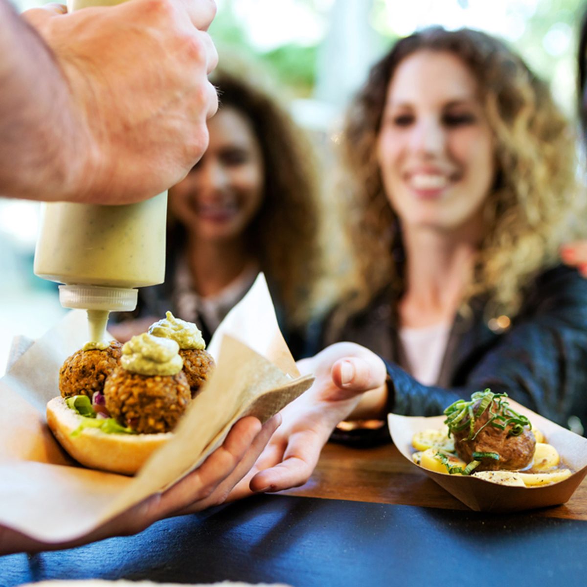 Portrait of three beautiful young women buying meatballs on a food truck in the park.