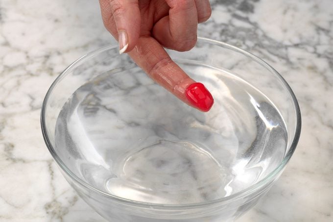 Testing red homemade candy using the cold water test. The mixture is flat after being removed from cold water, meaning it's in the soft-ball stage.