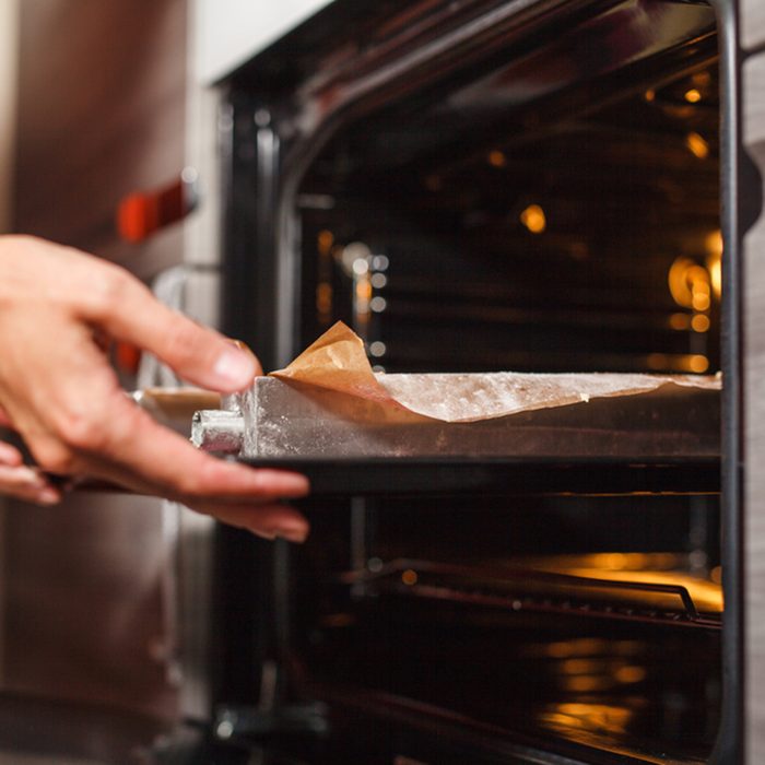 Woman cooking in the kitchen, puts cakes in the oven; Shutterstock ID 580824481