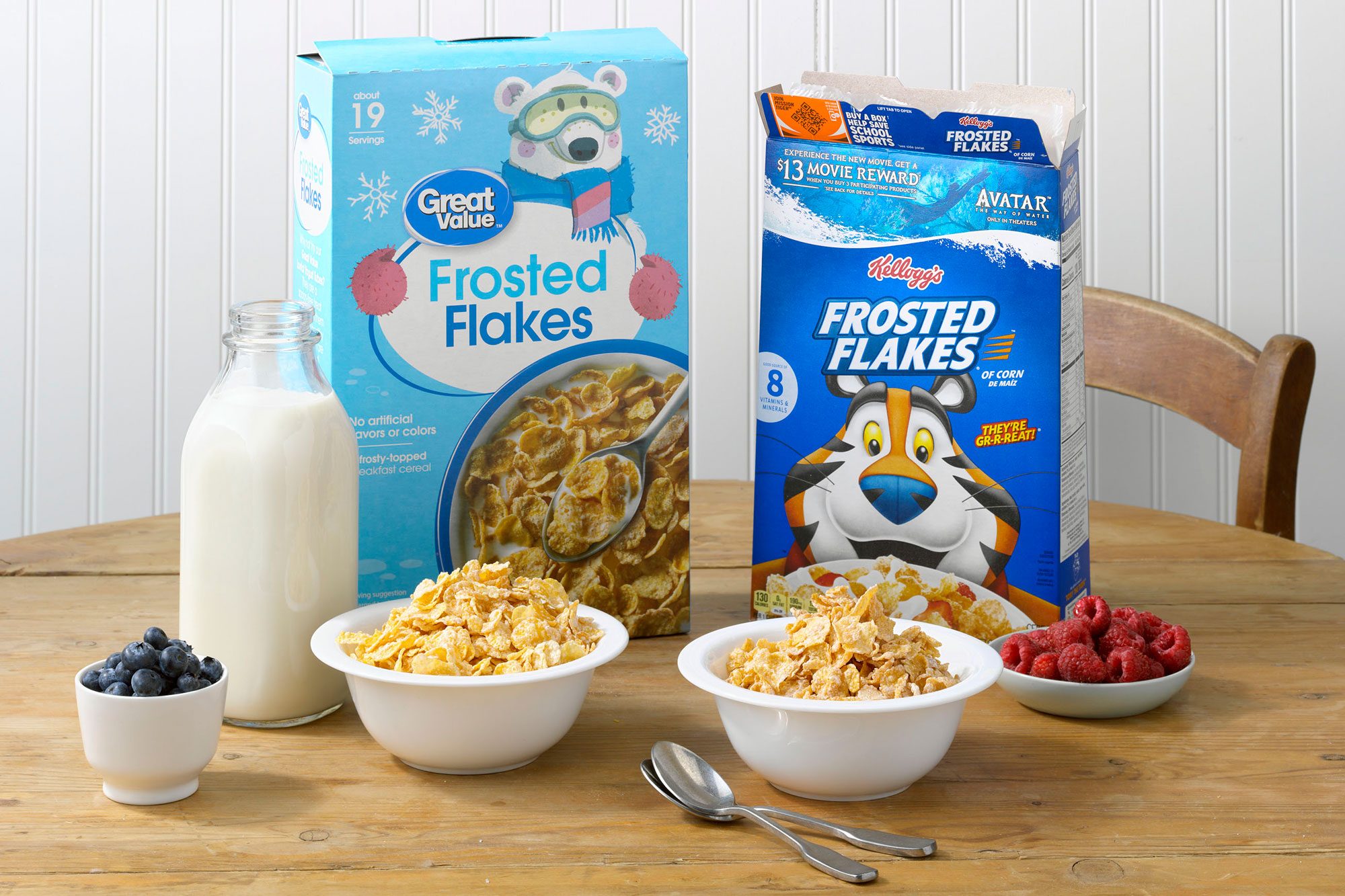 Kellogg's Frosted Flakes and Walmart's Great Value Frosted Flakes on a wood table with blueberries, raspberries, and milk