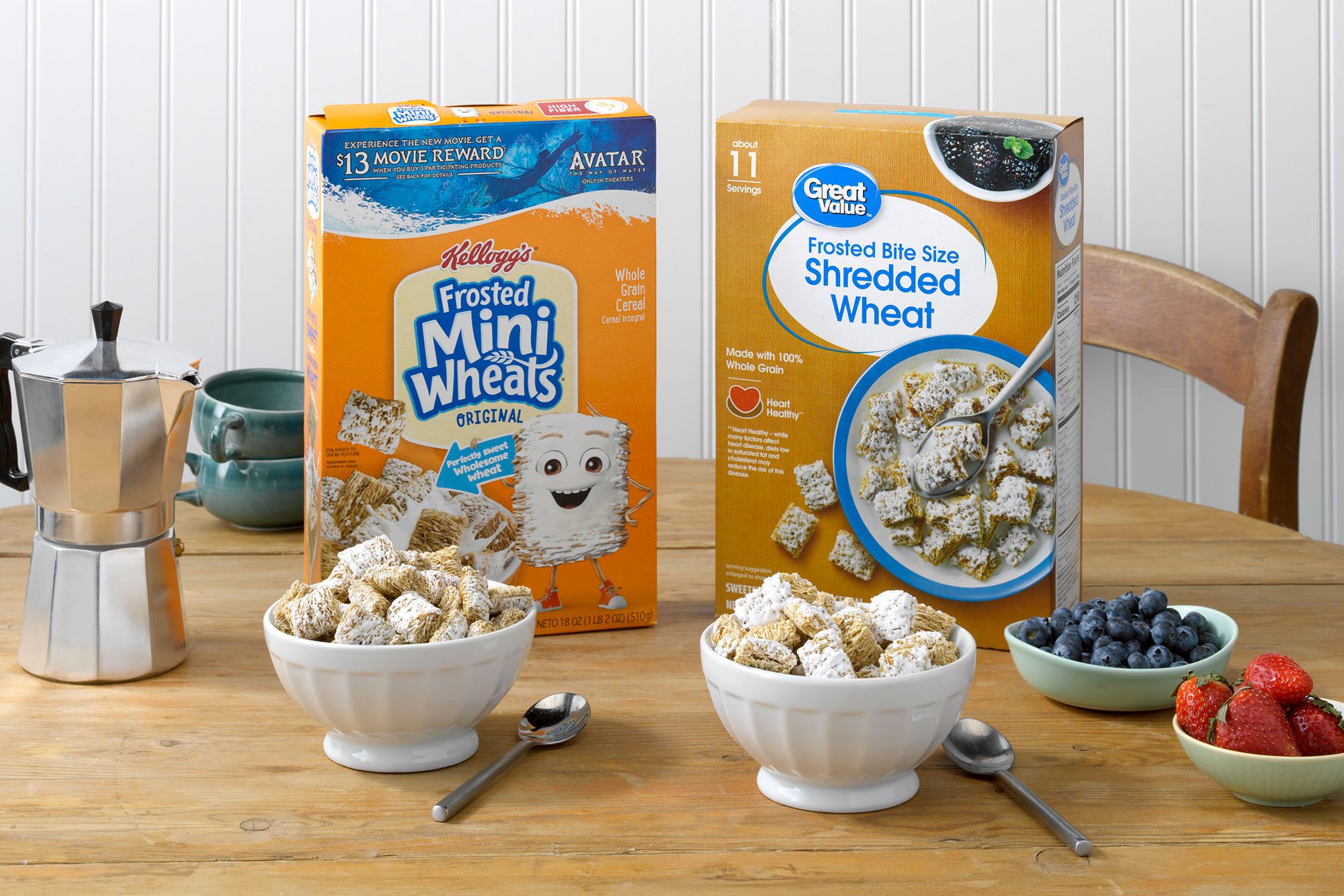 Kellogg's Frosted Mini Wheats and Walmart's Great Value Frosted Shredded Wheat on a table with coffee, blueberries, and strawberries