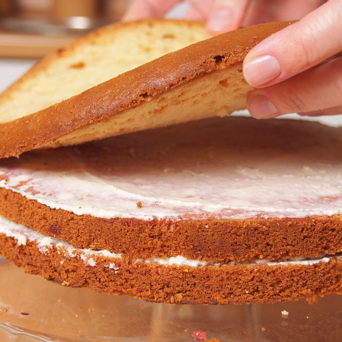 Stacking cake layers. Making torte with buttercream filling and grated chocolate topping.