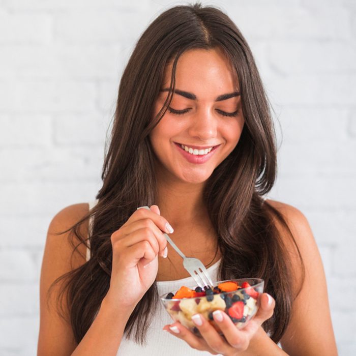Closeup Of Smiling Young Woman Eating Granola Fruit Parfait.