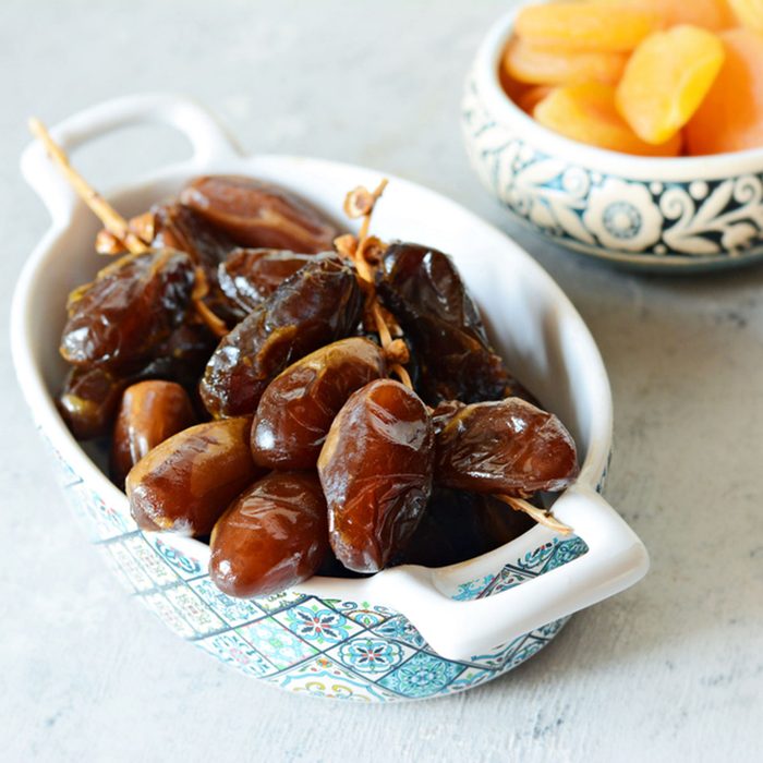 Bowls with juicy dates on a branch and dried apricots on a gray-blue background.