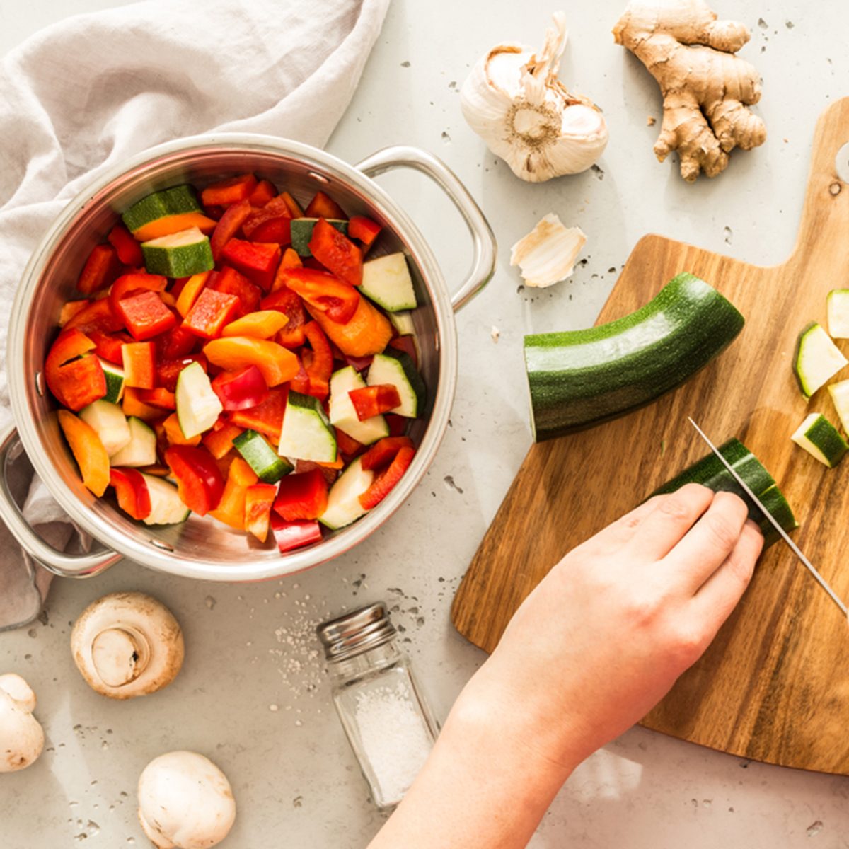 Cooking - chef's hands preparing vegetable vegetarian stew (thick soup). Kitchen scenery - pot with recipe ingredients around on the grey stone worktop captured from above (top view, flat lay).