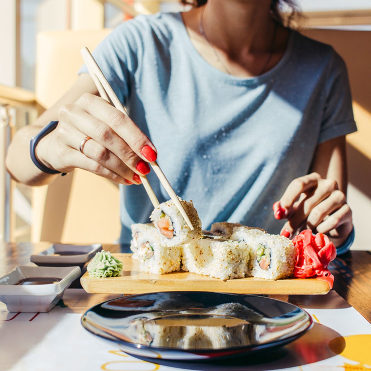 Woman in the blue shirt is eating at a sushi restaurant in summer