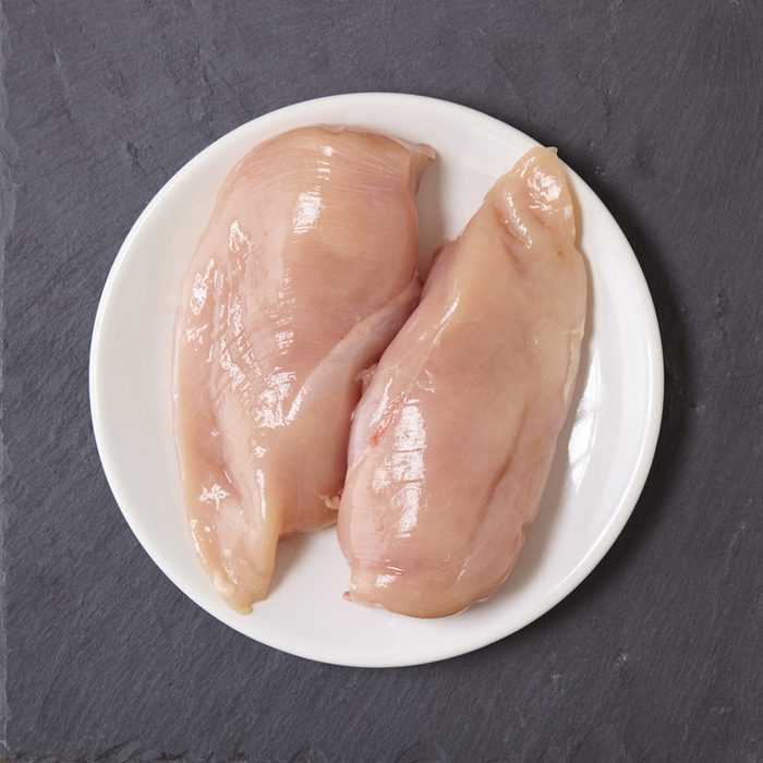 Food and raw meat - uncooked chicken breast fillets on a plate, on a rustic slate counter top background