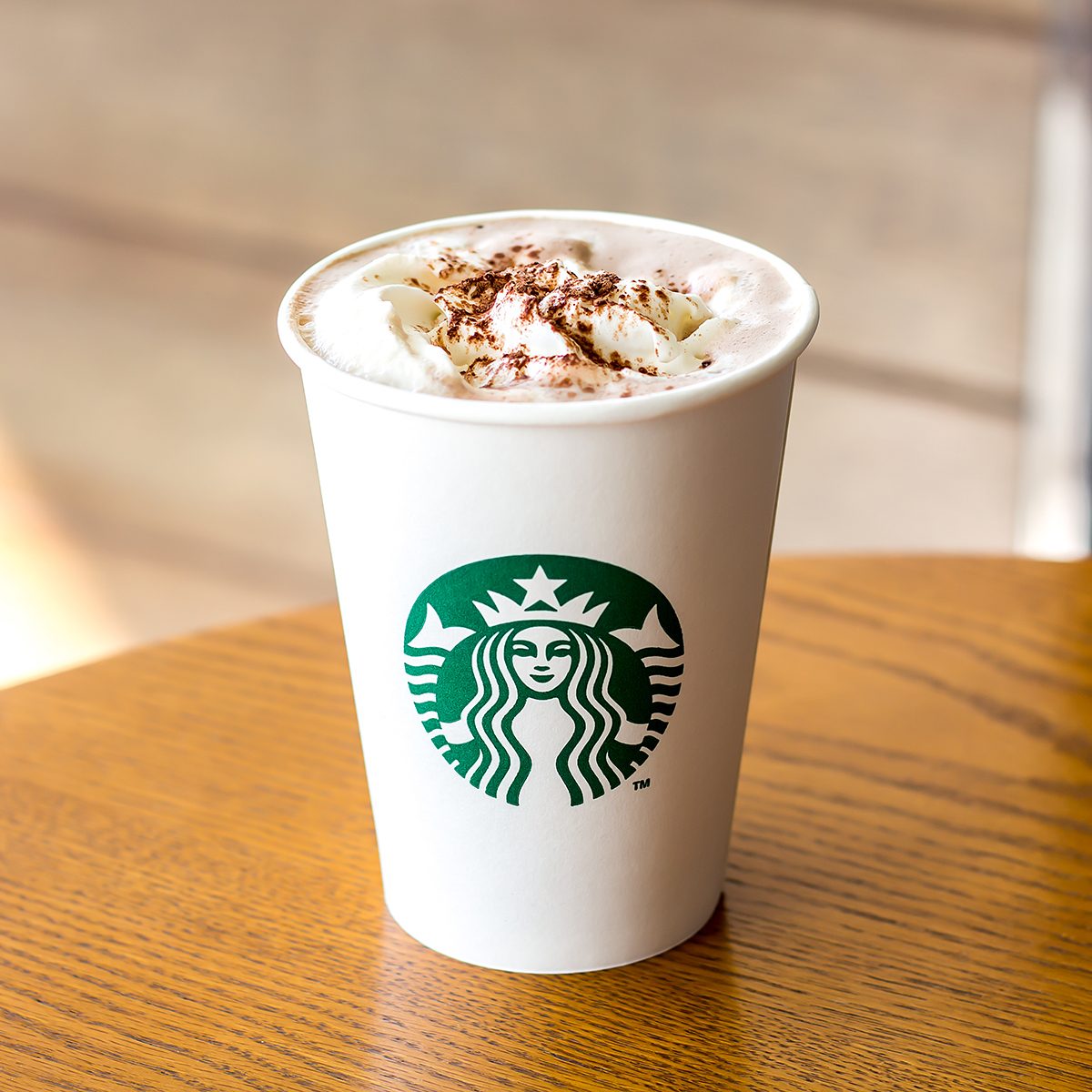 Starbucks Hot chocolate and whipping cream in white paper cup on wooden table