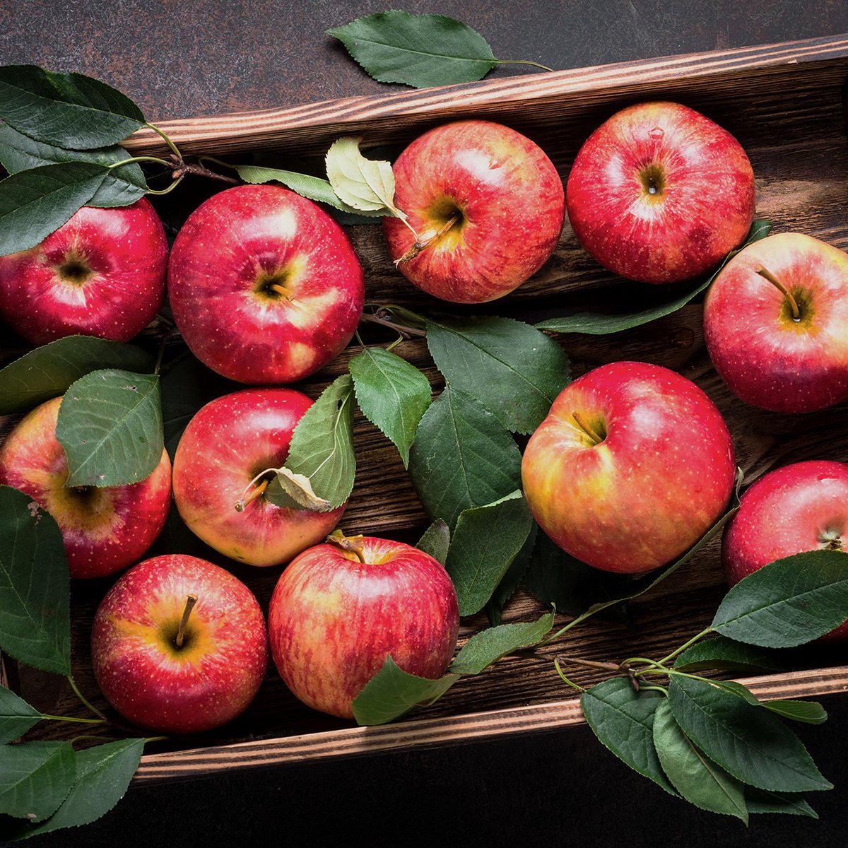 Red apples in wooden tray on dark stone table.