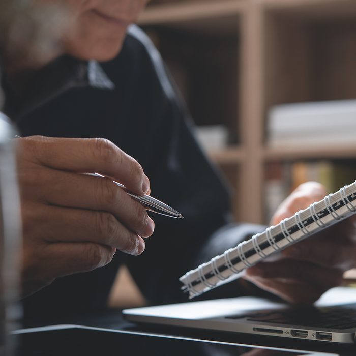 Asian business man holding pen reviewing business plan on notepad, working on laptop computer in office.