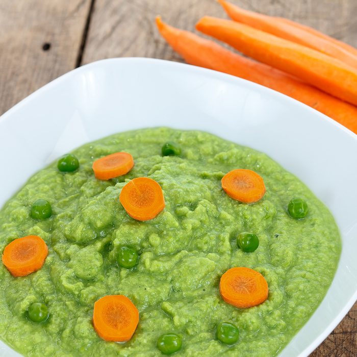Baby food with green peas and carrots on wooden table