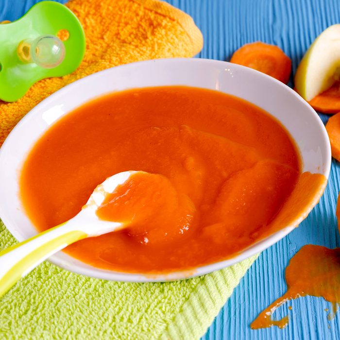 puree of baby carrot Apple on a wooden table spoon saucer white green pacifier napkin