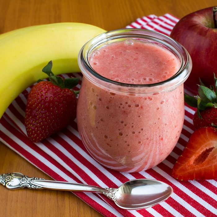 Puree with strawberry, banana and apple on the napkin on the wooden background