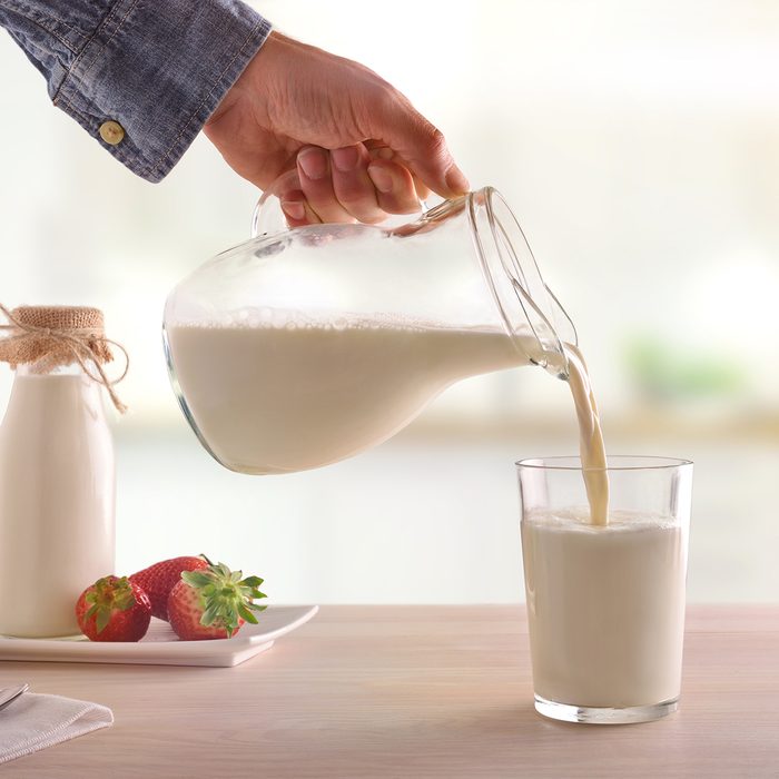 Serving breakfast milk with a jug in a glass on a white wooden kitchen table.