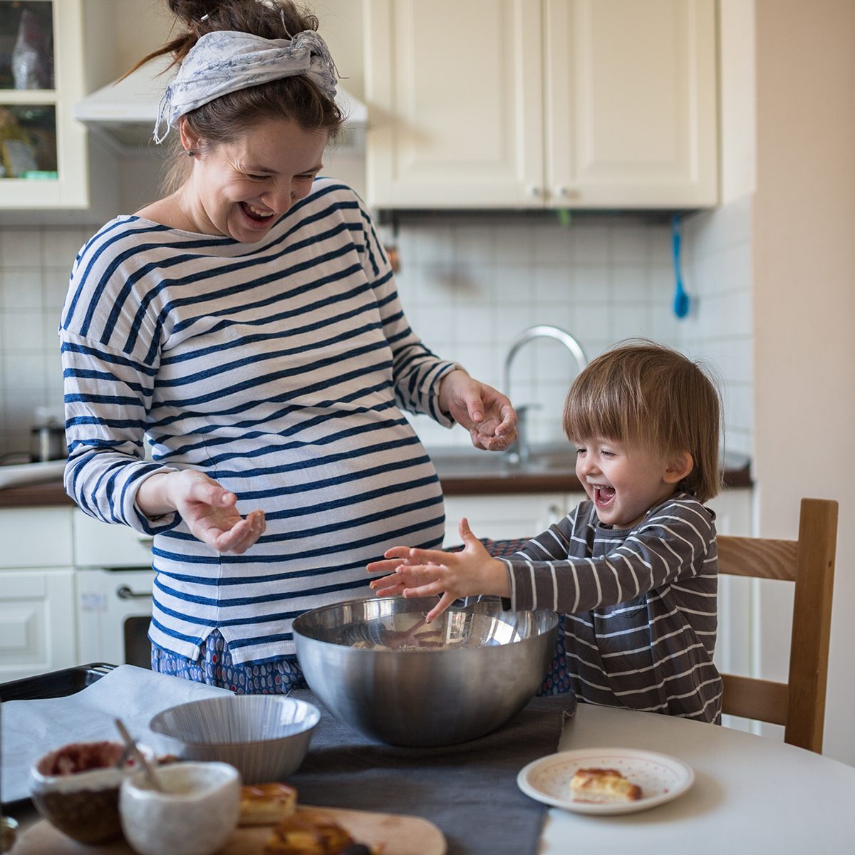 smiling young pregnant mother with dreadlocks is preparing in the kitchen with her son Toddler, dirty hands, make the dough for baking bread, lifestyle, toning, real interior