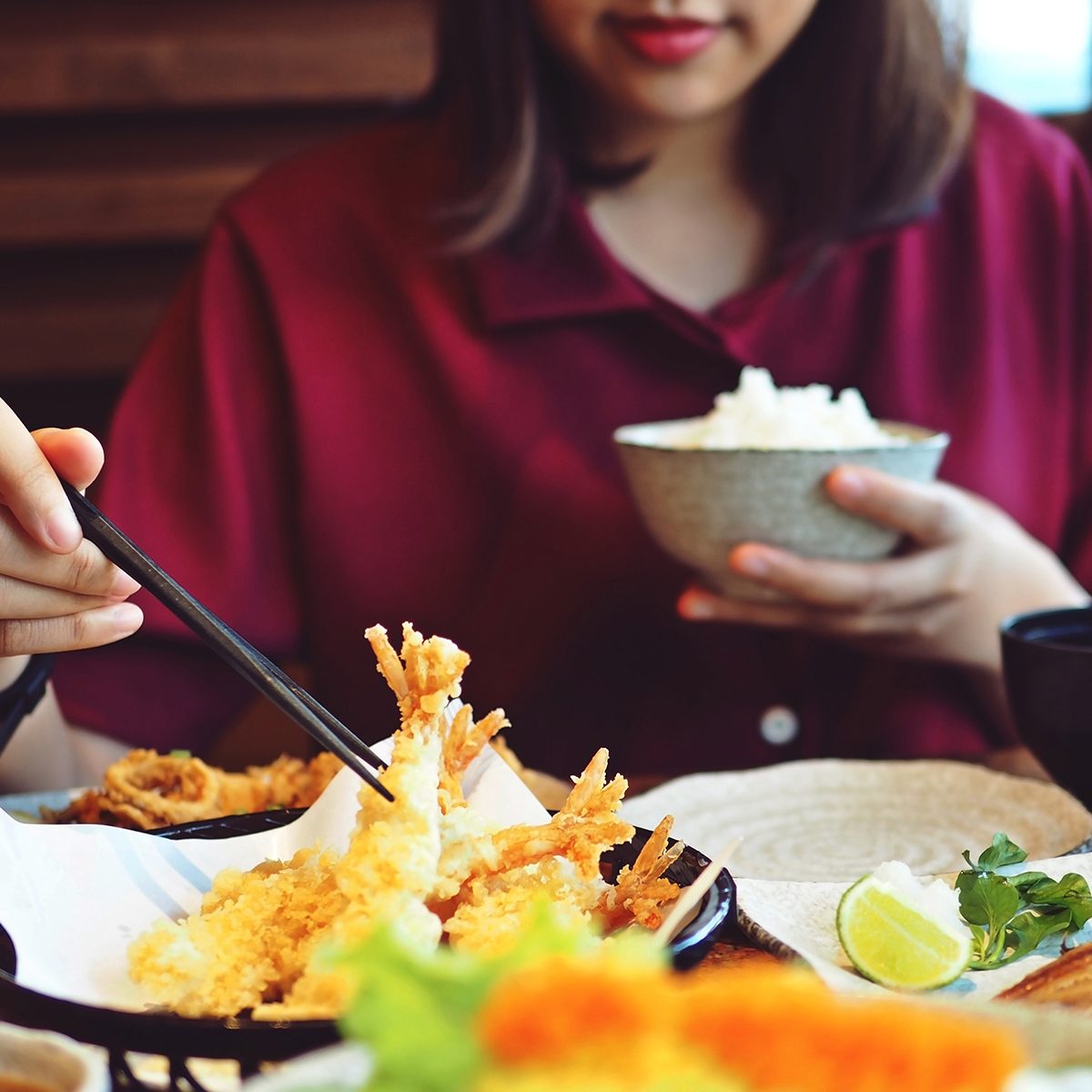 Young female hand using chopsticks to eat shrimp tempura with rice at restaurant. 