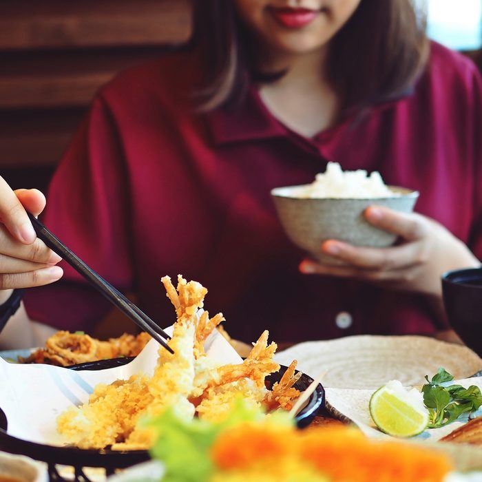 Young female hand using chopsticks to eat shrimp tempura with rice at restaurant.