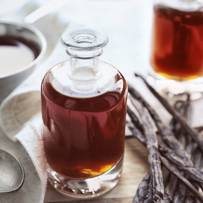 Bottle with aromatic extract and dry vanilla beans on table