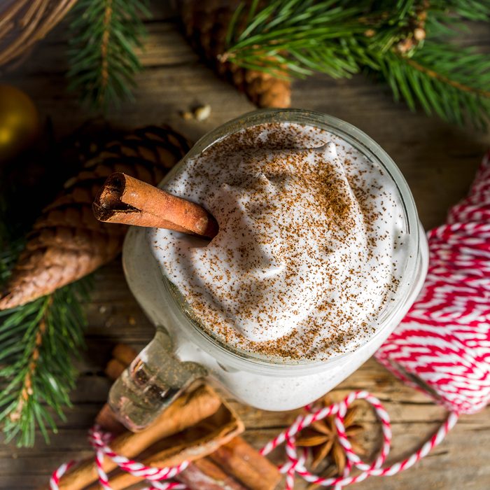 Christmas Tom and Jerry cocktail, whipped cream eggnog with spices, dairy milk beverage, with christmas decorations, rustic wooden background