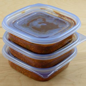 Batch of freshly made spaghetti sauce with ground turkey meat in plastic storage containers to prepare for freezer and meals in advance for work week