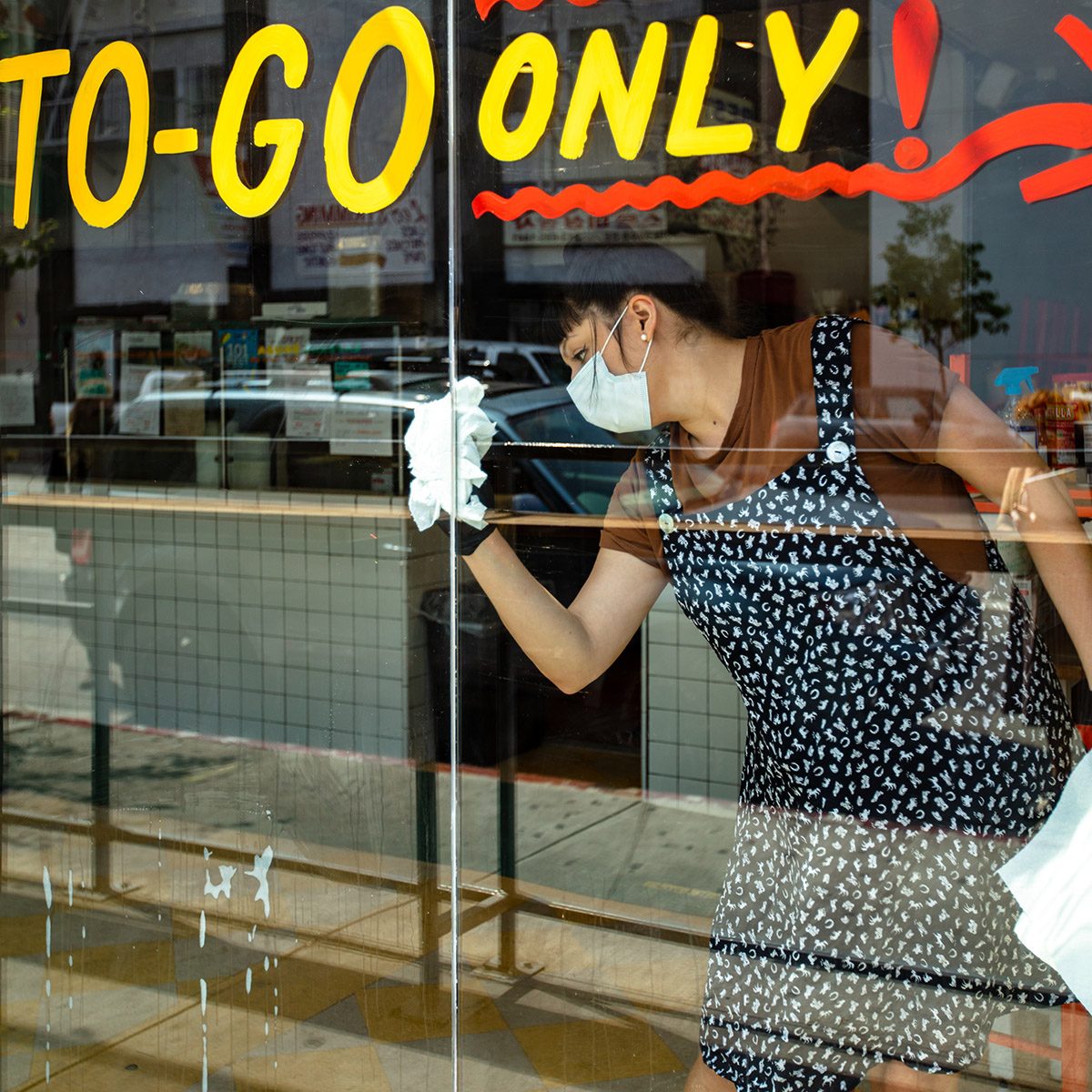 A Mexican restaurant adapts to the Covid-19 lockdown. The owner is cleaning the window wearing a mask and gloves.