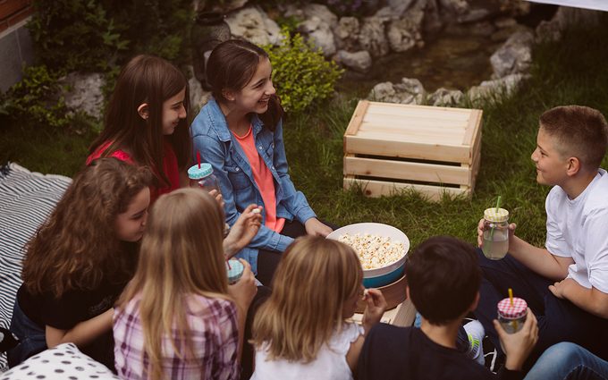 Group of children on movie night in backyard. Sitting, drinking lemonade and talking.