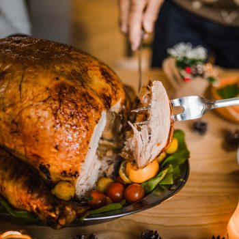 Close up of unrecognizable person carving white meat during dinner at dining table.
