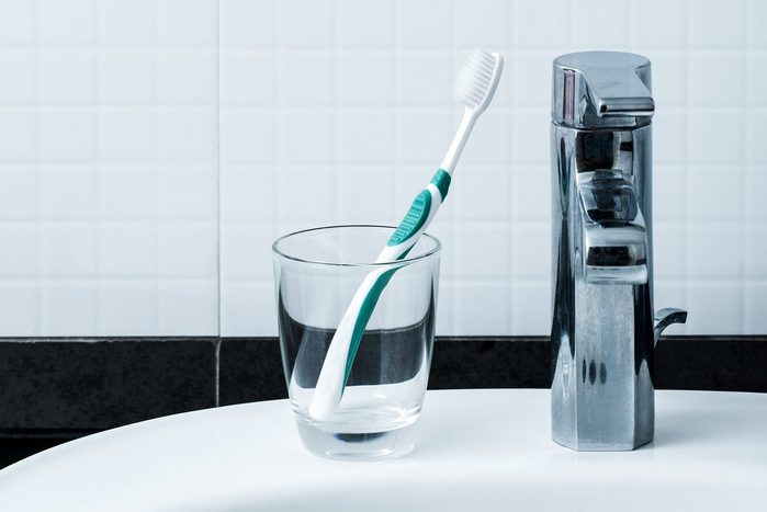toothbrush in a glass cup on the edge of a bathroom sink