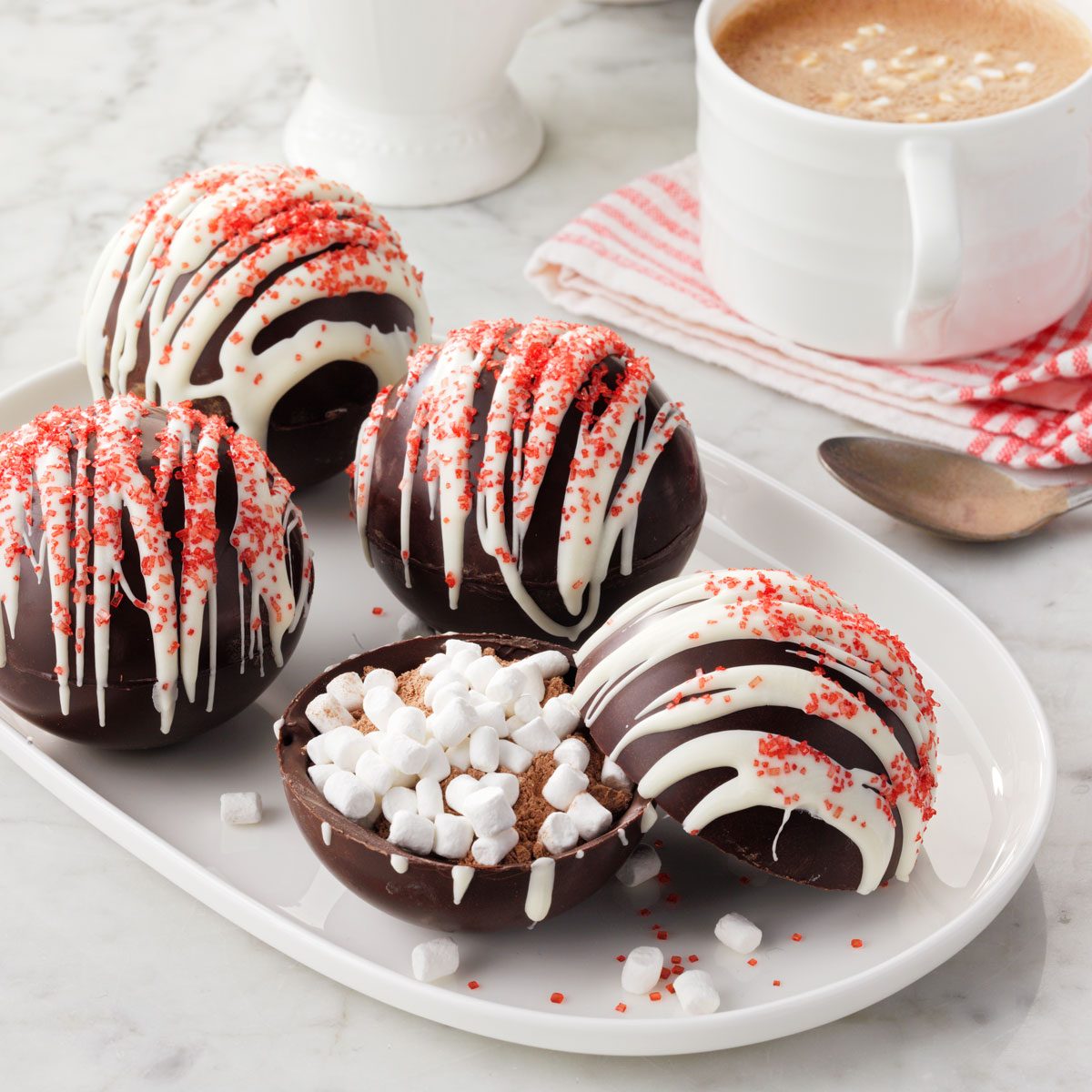 Hot Chocolate Bombs arranged on a white tray with a cup of hot cocoa in the background