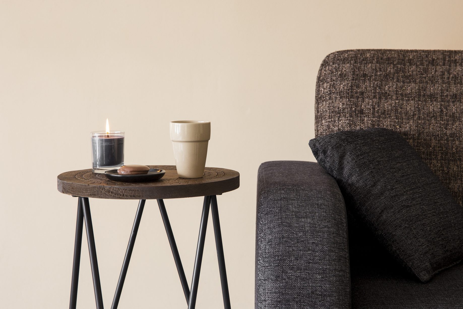 Detail view of modern round wood metal coffee table with cappuccino mug, glass candle burning by the side of sofa.