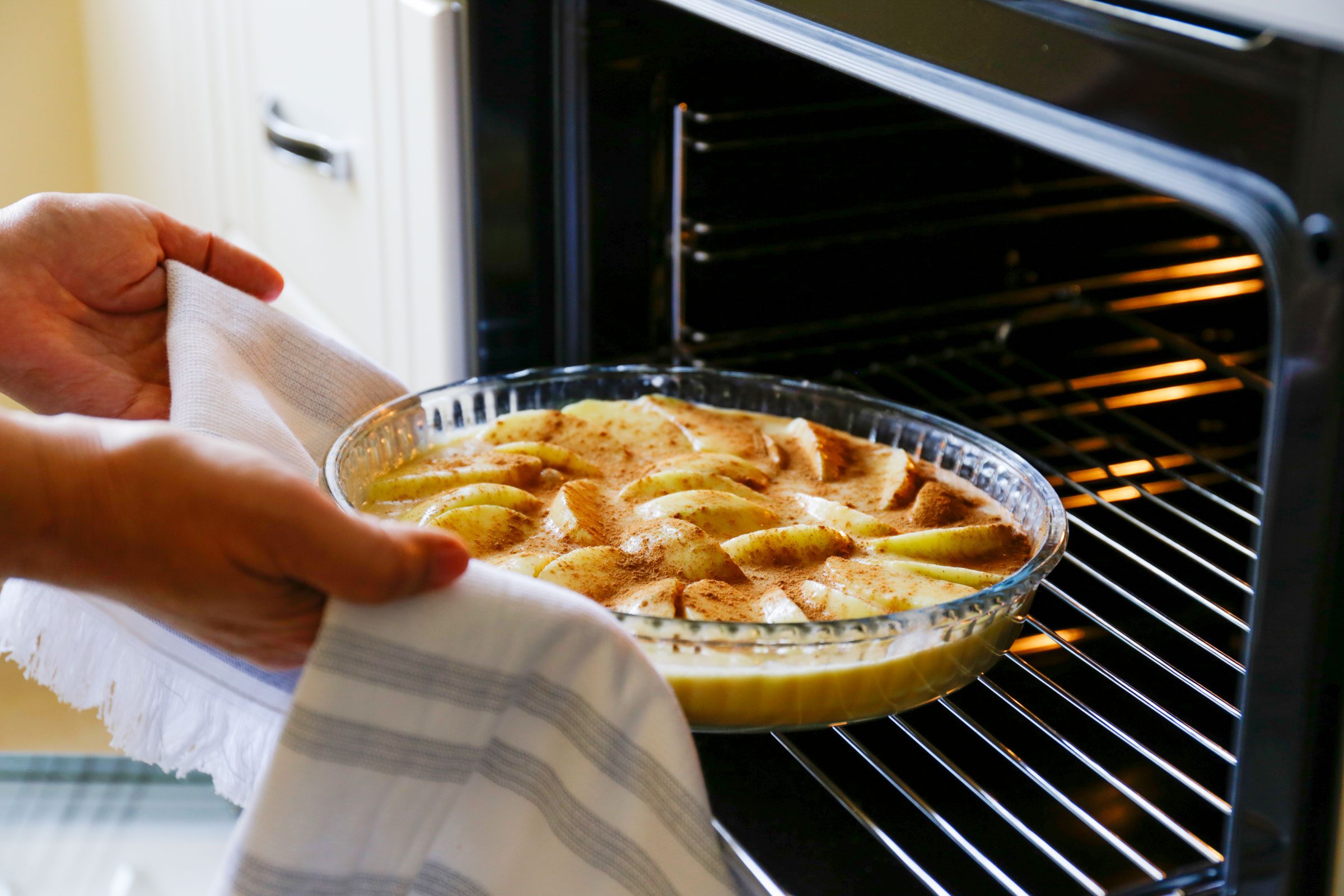 person placing a tart in a glass dish into an open oven