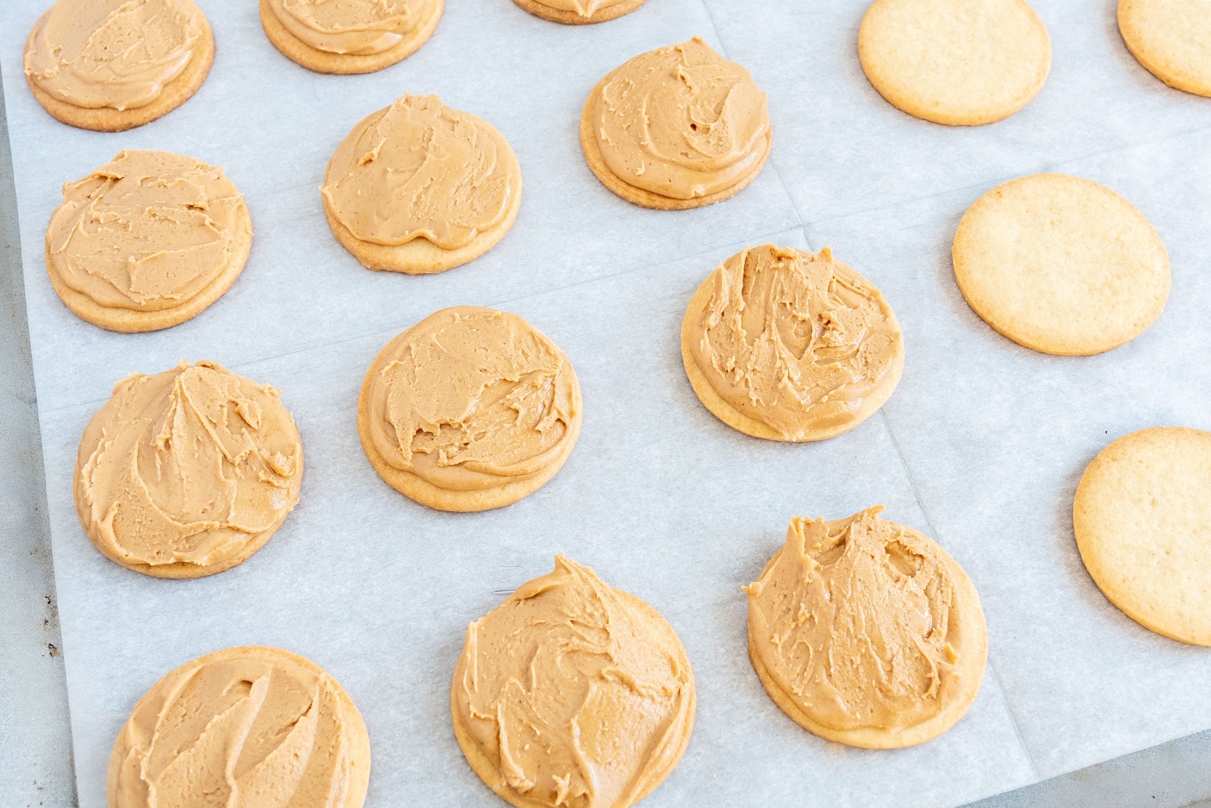Tagalongs on a baking sheet; some have peanut butter topping, some do not yet have peanut butter topping