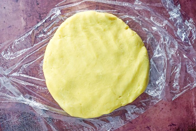 flattened disk of dough on a sheet of plastic wrap on a purple background