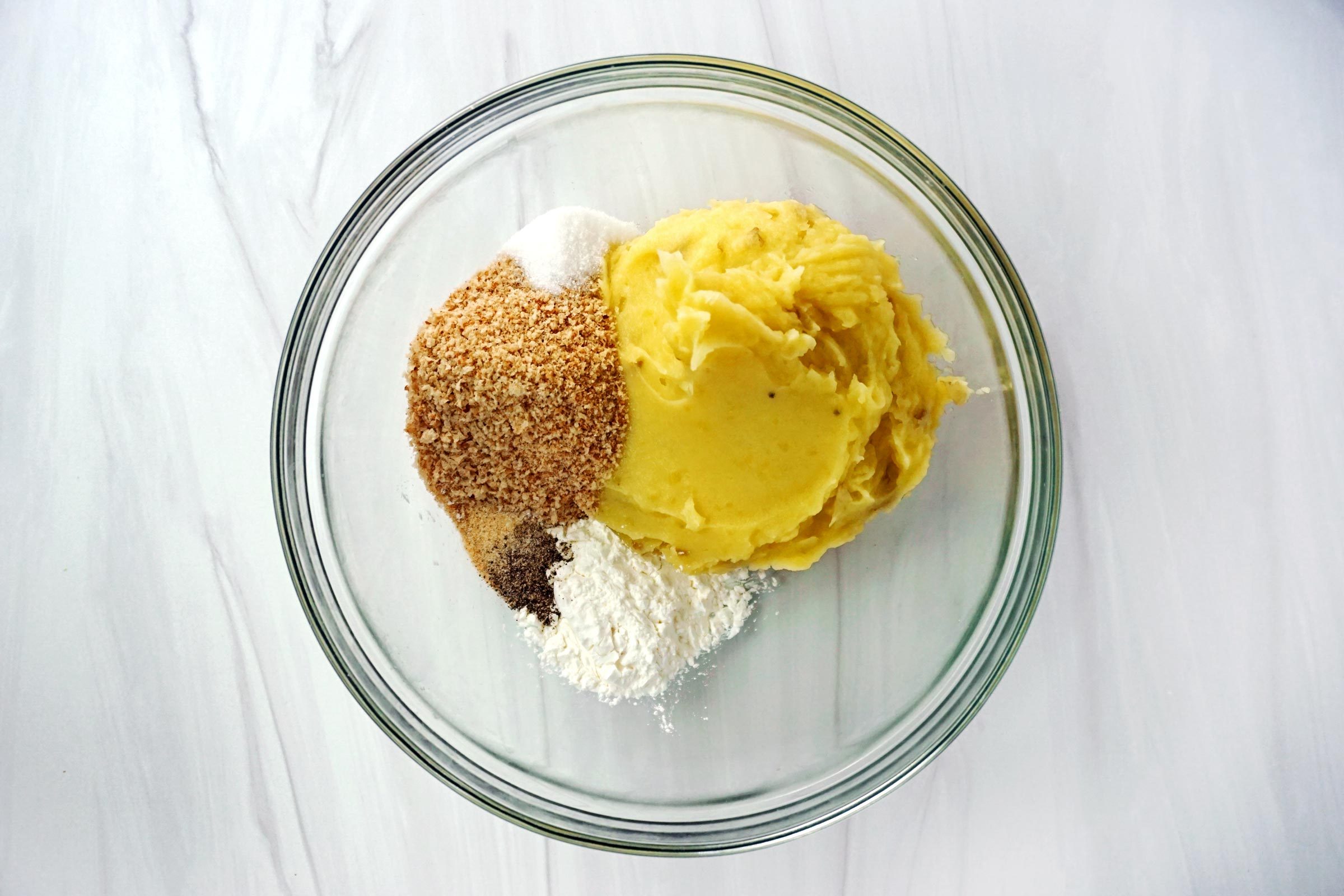 mashed potatoes and other spices piles in a clear bowl on a white table cloth, view from above