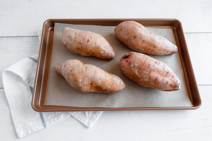 four whole sweet potatoes on a baking sheet