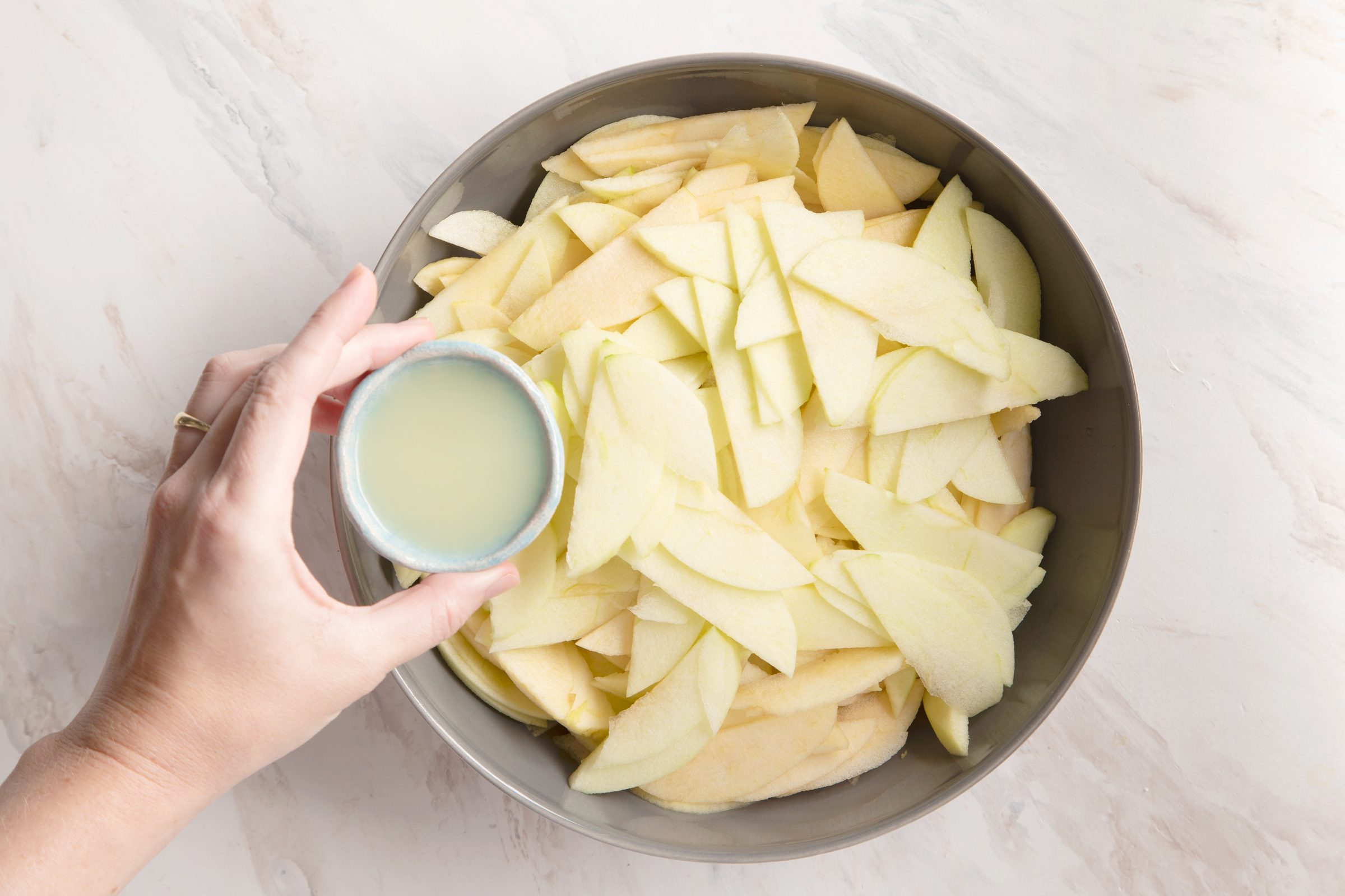 adding lemon juice to a bowl of sliced apples