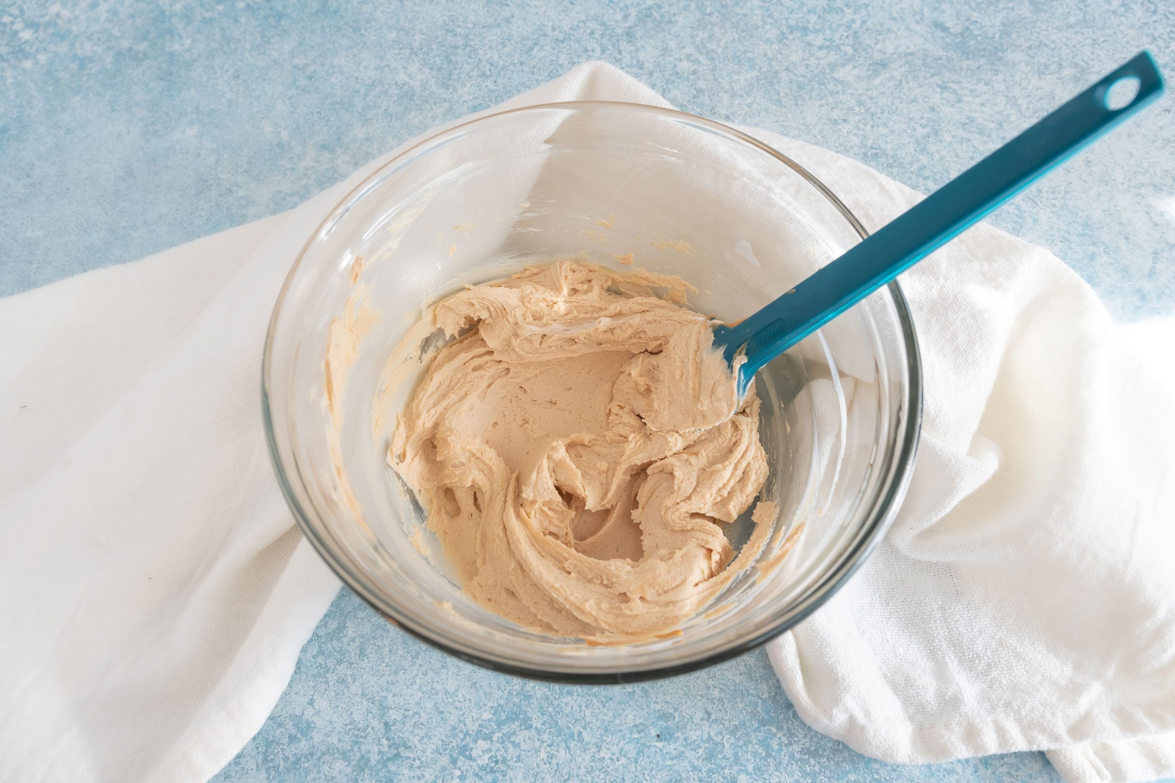 mixing frosting for dog cupcakes a glass bowl with a rubber spatula on a blue countertop