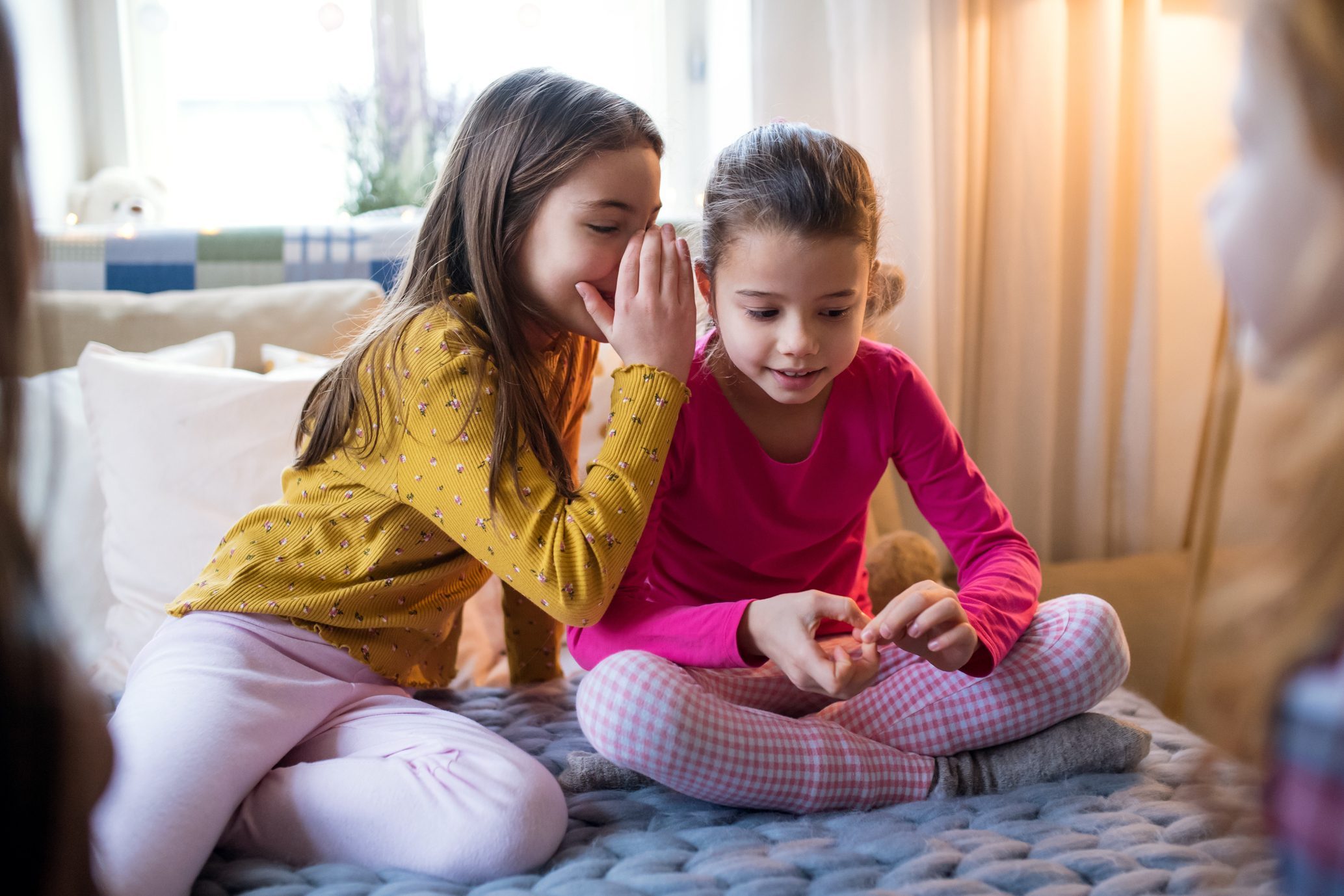 Group of small girl friends sitting and playing on bed, having good time.