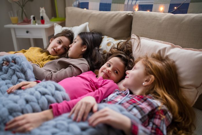 Group of small girl friends lying in bed, talking.