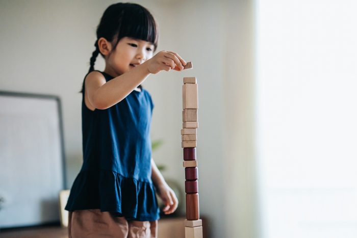 Creative little Asian girl having fun playing wooden building blocks at home. Learning through play concept