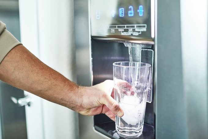Unrecognizable man filling glass from refrigerator water dispenser