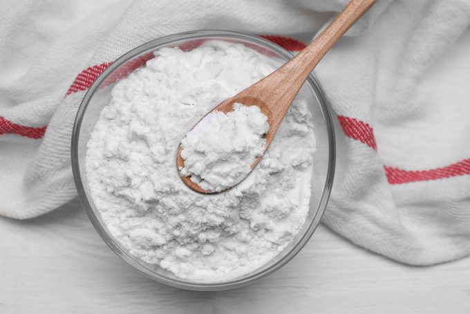 Bowl and spoon of starch on white wooden table, top view