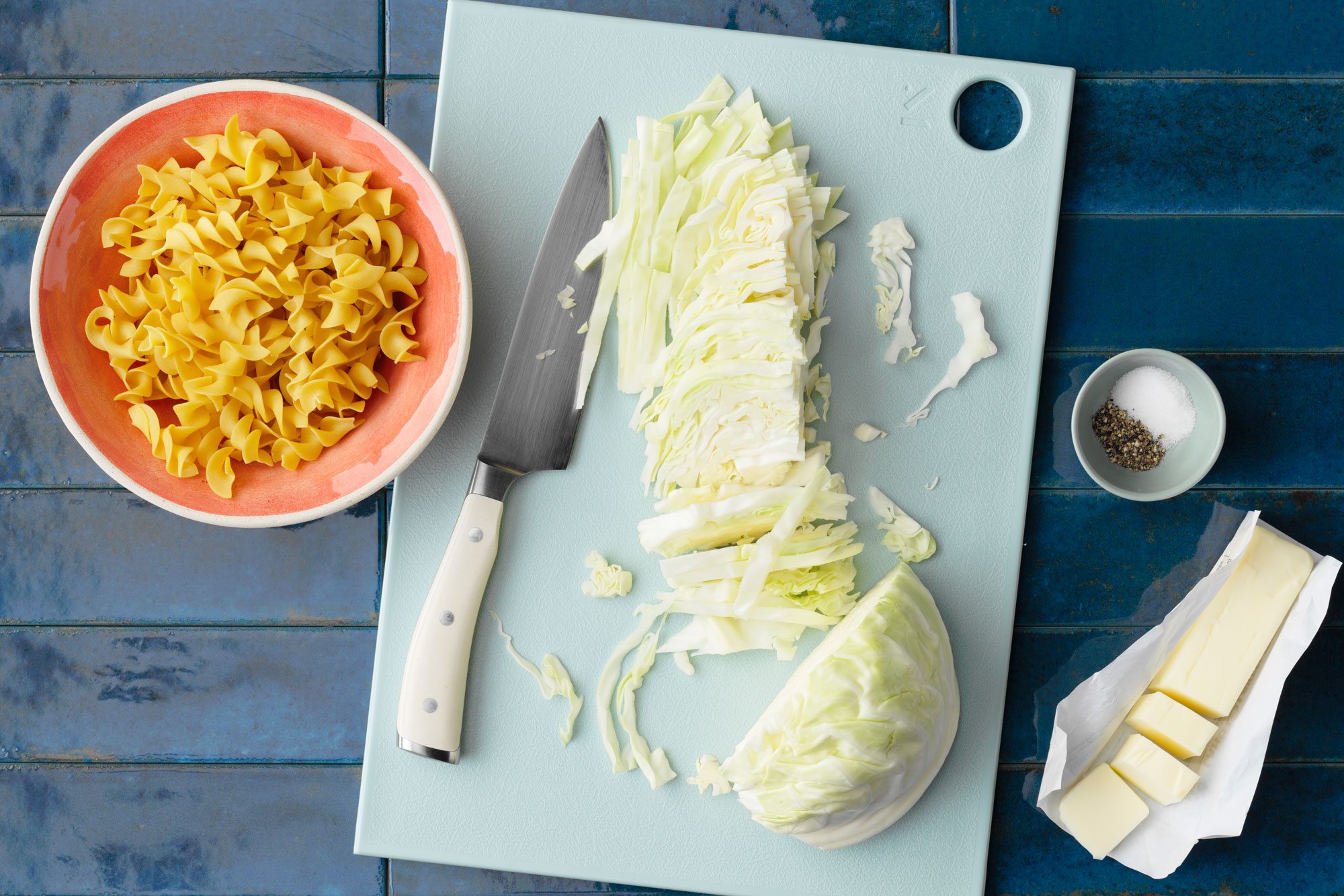 haluski Cabbage and Noodles Overhead Shot Of All Ingredients On dark blue tiled Surface.